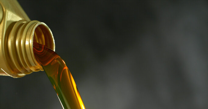 Close-up of motor oil pouring from a plastic container. Golden viscous liquid with bubbles flowing smoothly, automotive maintenance concept with shallow depth of field.