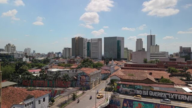 Drone ascent over downtown Cali revealing the iconic Torre de Cali, the city's tallest building. View includes colorful street art murals, colonial rooftops, and modern office towers in Versalles.