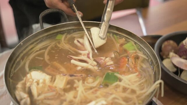 Close up hands cutting squid from spicy seafood noodle soup most popular Korean food in restaurant 