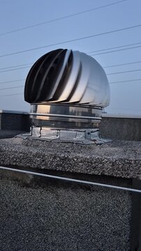 Rooftop terrace concrete floor with stainless steel vent caps and chimney pots in motion, filmed outdoors at sunset on a modern building.