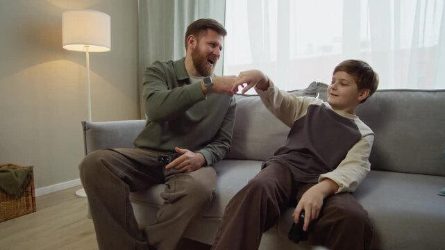Long stab POV shot of excited gen Alpha kid fist bumping with Caucasian father while playing video games with controllers in living room