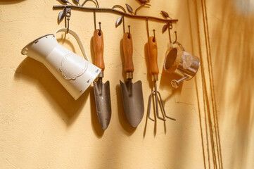 Miniature gardening equipment including a rake and trowels hanging on a rustic hook. © Anna