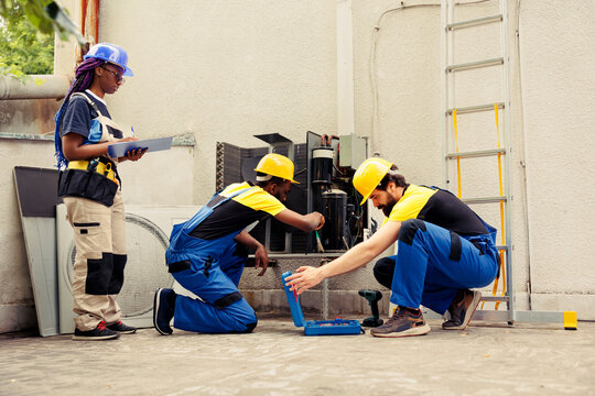 Diverse crew contracted by home owner to fix broken air conditioner. Coworking mechanics analysing broken blower fan causing frozen evaporator coil, resulting in poor airflow