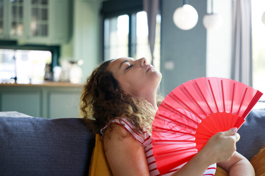 Woman feeling relief using hand fan during hot weather at home