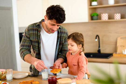 Father helping daughter spread jam on toast during breakfast