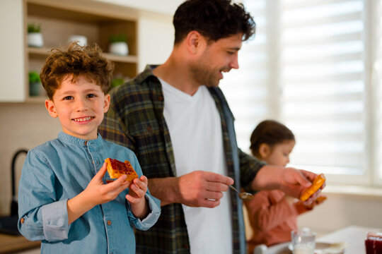 Smiling boy holding toast with jam while standing in kitchen