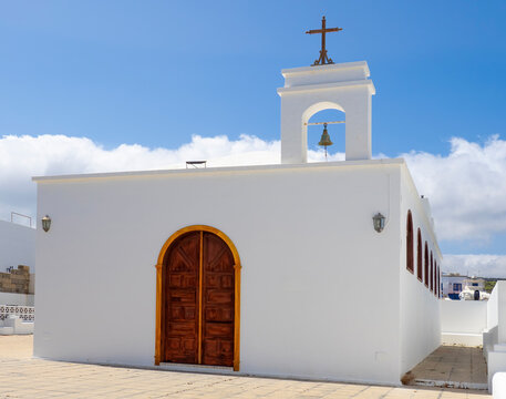 small white chapel in punta mujeres lanzarote with wooden door bell tower cross and blue sky in a quiet village setting