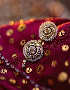 Macro close-up of kundan bridal earrings on deep crimson silk with scattered gold sequins, highlighting intricate craftsmanship for jewelry advertising and premium wedding editorials
