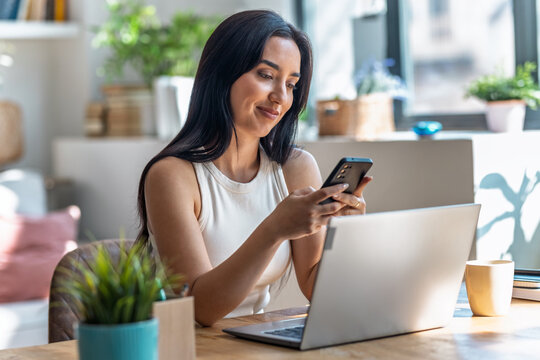 Beautiful woman using smartphone while working with laptop in the livingroom at home