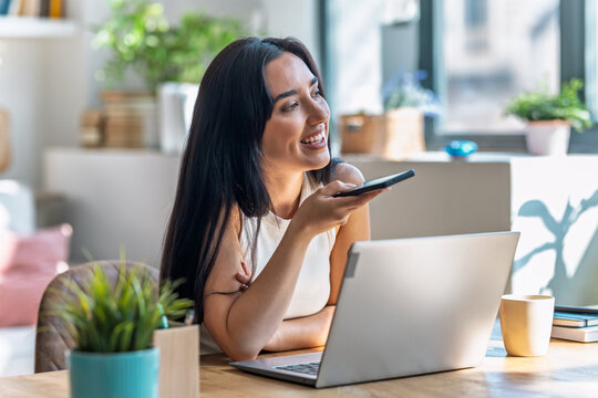 Beautiful woman using smartphone while working with laptop in the livingroom at home