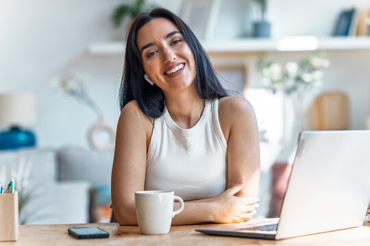 Beautiful woman looking at camera while working with laptop in the livingroom at home