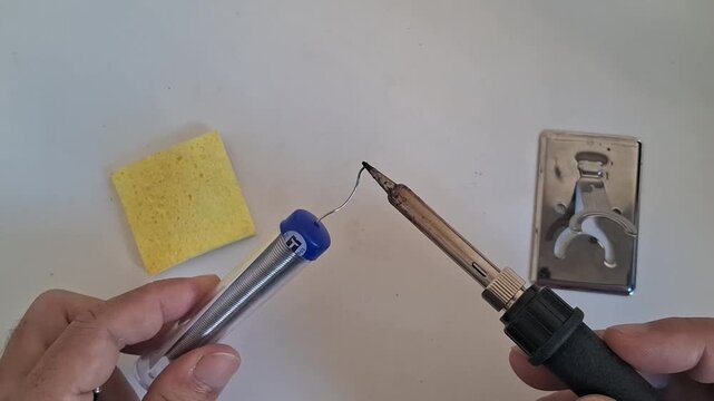 Close-up of hands holding a hot soldering iron and solder wire for electrical repair footage.