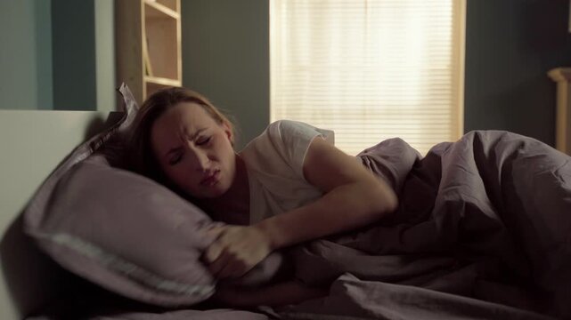 Stressed young woman suffering from insomnia, struggling to find a comfortable position in bed, tossing and turning with anxiety and exhaustion during a restless night at home