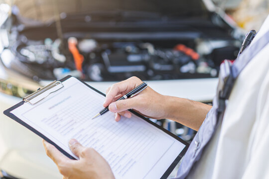 Auto check, car service shop concept. Automobile repairman writing job checklist on clipboard, mechanic checking engine to estimate repair machine, inspecting maintenance by engineer at vehicle garage