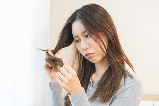 Damaged Hair, frustrated asian young woman, girl hand in holding splitting ends, messy unbrushed dry hair with face upset, long disheveled hair, health care of beauty. Portrait isolated on background