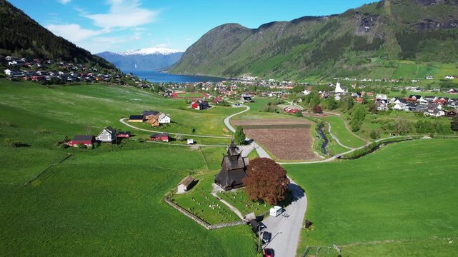 Urnes Stave Church near farms and green hills in Norway with fjord in background