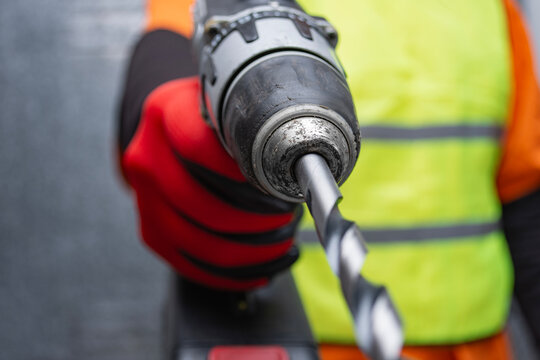 Builder holding a cordless power drill machine. Concept of precision engineering, industrial renovation, manufacturing and safety equipment at work with selective focus on drilling bit.