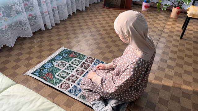 Saudi Arabia woman sitting on prayer rug in home interior during Ramadan