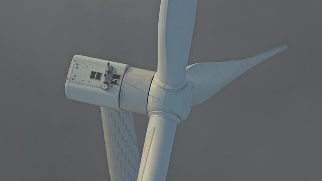 Close up view of a massive wind turbine rotor turning slowly in dense fog. The white nacelle and spinning blades generate clean electricity