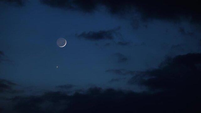 Blue hour time with crescent Moon, stars and planets above landscape silhouettes.