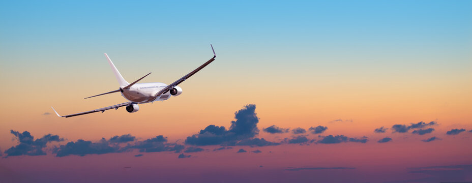 Airplane flying into colorful sunset sky at dusk