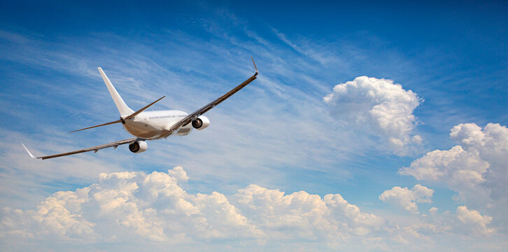Airplane flying in clear blue sky with fluffy clouds