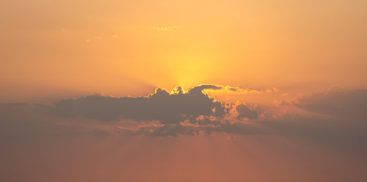 Dramatic golden sunset with sun rays piercing through dark clouds panorama.
