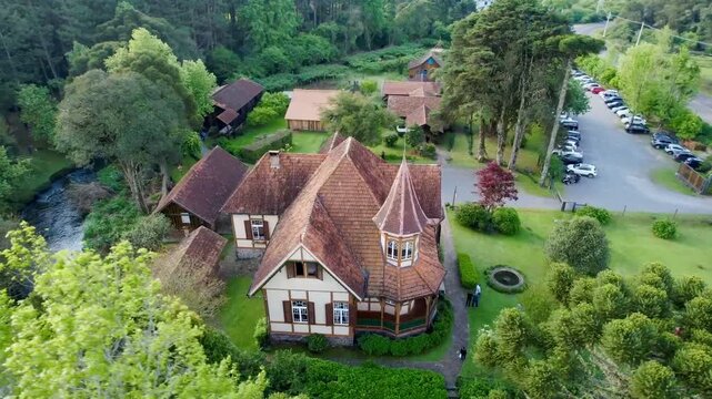 Aerial drone close up view of European style chalet with brown roof surrounded by trees in Gramado Brazil