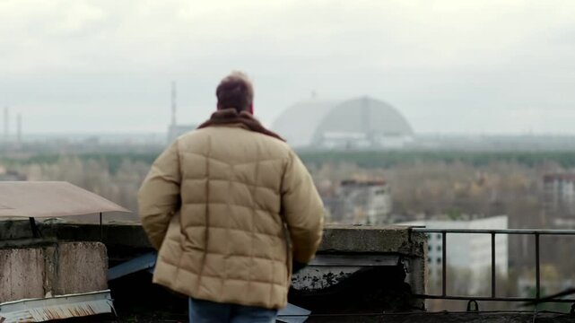 Man walking on a Pripyat rooftop viewing the Chernobyl New Safe Confinement sarcophagus