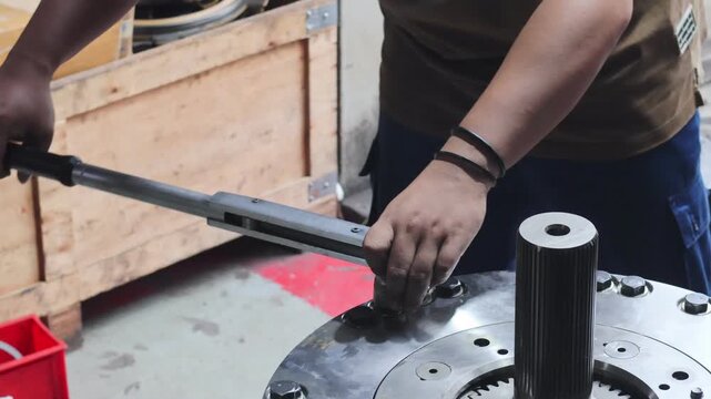 A close-up shot of a technician&rsquo;s hands using a heavy-duty torque wrench to tighten bolts on a large industrial transmission assembly in a workshop.