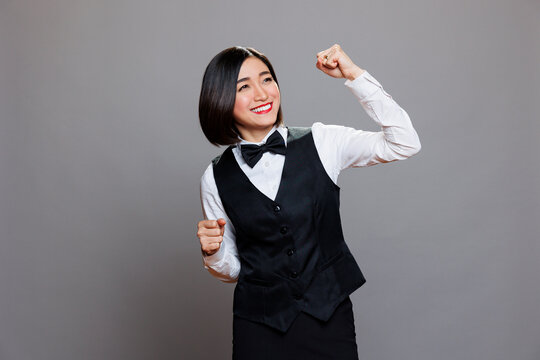 Cheerful asian waitress dressed in restaurant uniform dancing with joyful facial expression. Cafe smiling woman employee making moves with hands and body, spreading happiness