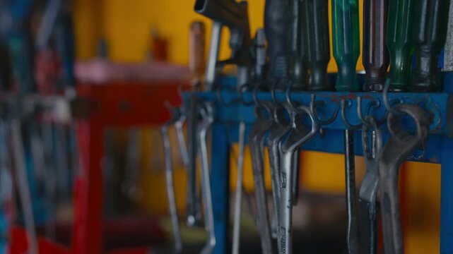 Tool storage rack with wrench and screwdriver hanging in workshop interior, metal hand tools on storage rack, repair work and garage tool handling with blurred hands