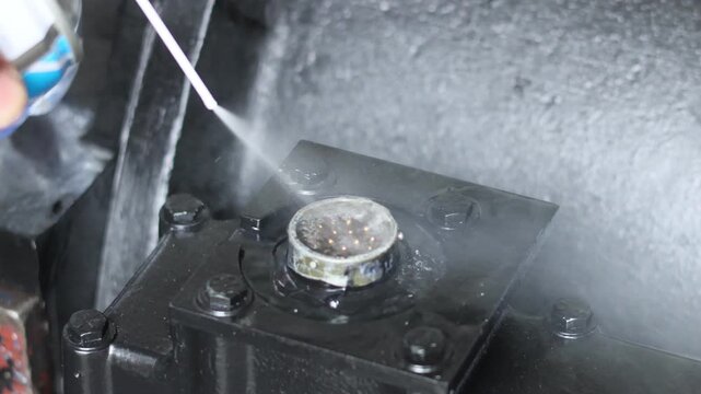 A close-up shot of a technician using a specialized contact cleaner spray to remove dust and oxidation from a multi-pin electrical connector on industrial machinery.