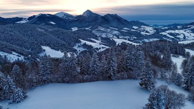 Aerial hyperlapse orbit of snow covered winter mountain landscape at dusk