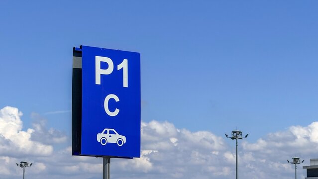 Blue parking sign with car icon and P1 C lettering, outdoor lot setting under bright sky and clouds, clear wayfinding for drivers, travel and transport theme