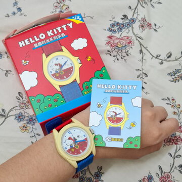 Sanrio Hello Kitty Character Wristwatch for Kids Displayed with Original Packaging Box and Collectible Card on Floral Pattern Fabric Background on December 26, 2025 in Bangkok, Thailand