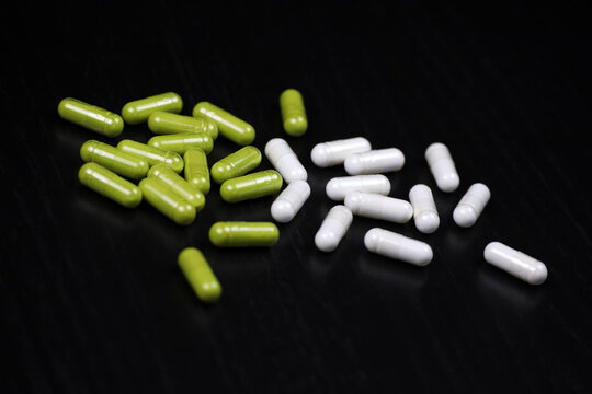Pills in white and green capsules scattered on a black wooden table. Background for herbal medicine, antibiotics, vitamins, dietary supplements