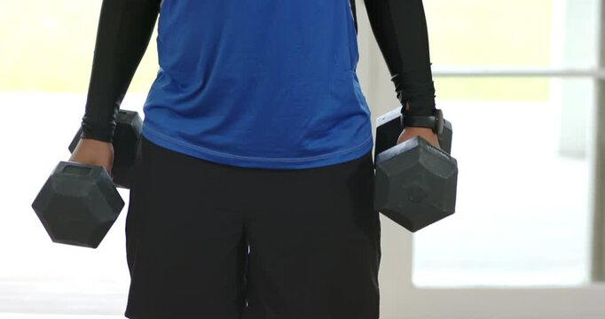 Camera panning upward showing adult man performing alternating dumbbell curls for workout at home