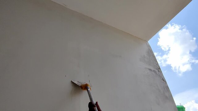 Worker applies putty on high wall using old tool