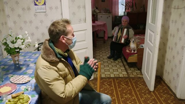 Visitor listening to an old woman playing the accordion inside her home in Pripyat, Ukraine