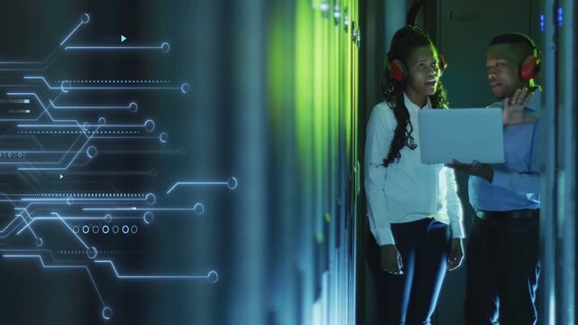 Man raising laptop, woman watching, both debugging server racks while circuit overlay mapping data
