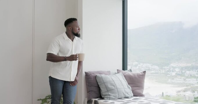 Window view urging man in white-shirt in apt holding mug sipping leaning walking right, copy space