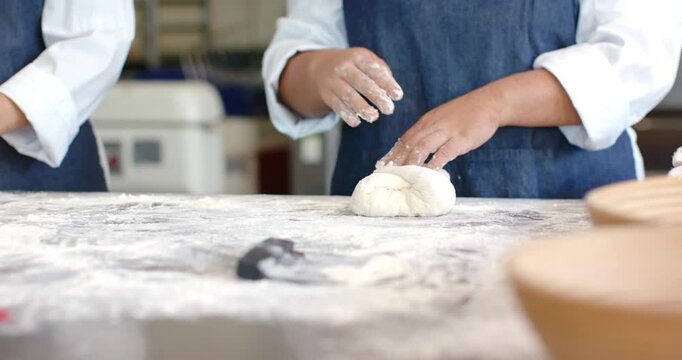 Vertical video: Female baker picking up dough end, folding and pinching on floured bench for baking