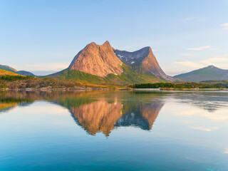 Mountain peaks reflecting in the calm fjord water during midnight sun in Norway. Scenic arctic summer landscape with golden hour light and northern nature. © biletskiyevgeniy