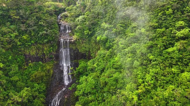 Aerial view of a stunning multi-tiered waterfall cascading through the lush tropical jungle of Mauritius with morning mist