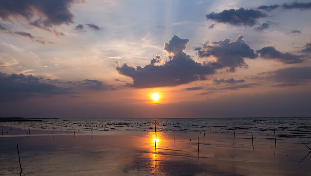 Dramatic golden sunset with sun rays over calm sea reflection panorama.