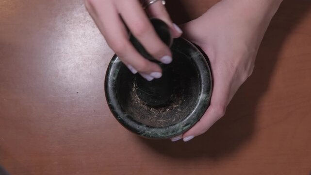 A girl grinding spices in a mortar and pestle at the kitchen table