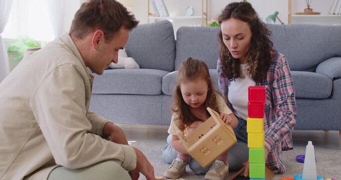 Parents and family play with daughter and toys. At home on carpet, they build blocks and a wooden house, boosting creativity and motor skills. Family leisure, bonding and learning together.