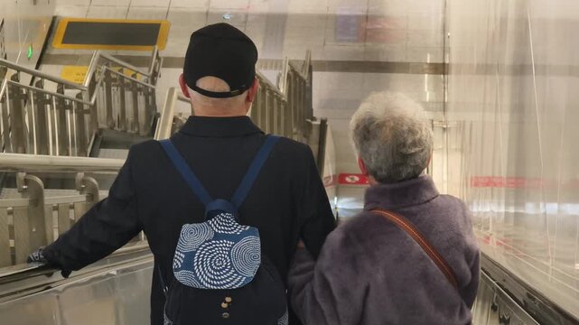 Elderly Woman and Companion Using Escalator in Subway Station, Beijing, China.
