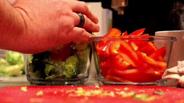 Hands organizing fresh broccoli and red bell pepper in glass containers for healthy meal prep